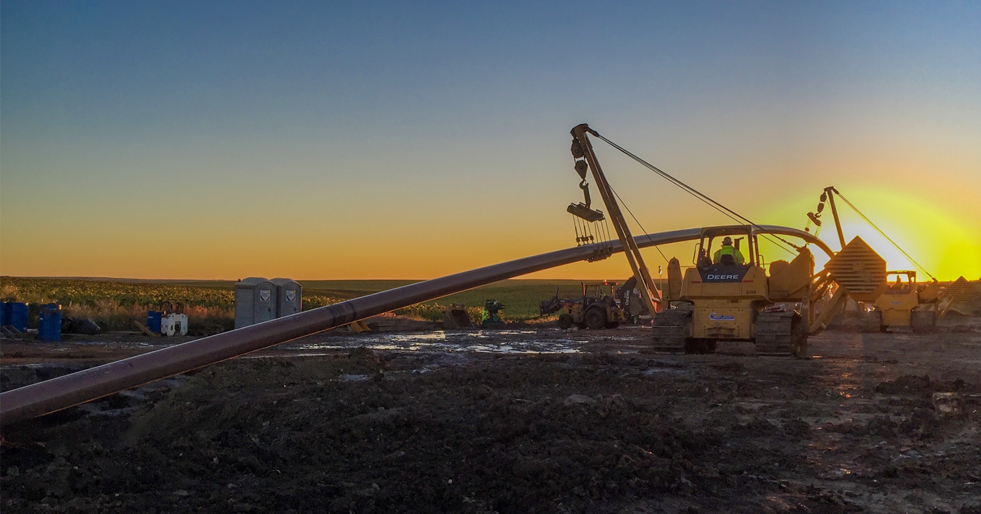 Pipe layer laying pipe into ground at dusk