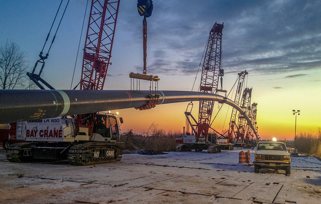 Several cranes holding up large pipeline during sunset